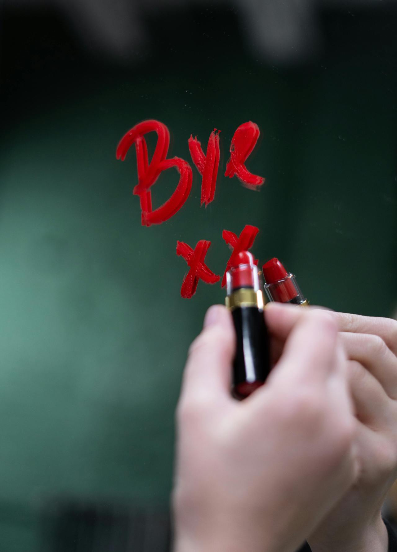The word "Bye" followed by two Xs written in red lipstick on a mirror.