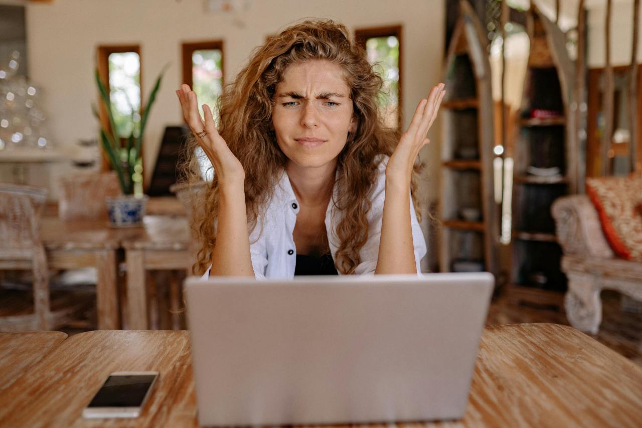 A woman with curly hair stares at her laptop screen looking puzzled and upset.