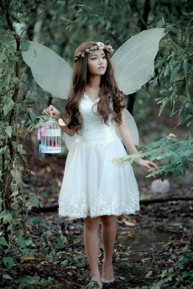 A woman dressed as a fairy carries a lantern in the woods.