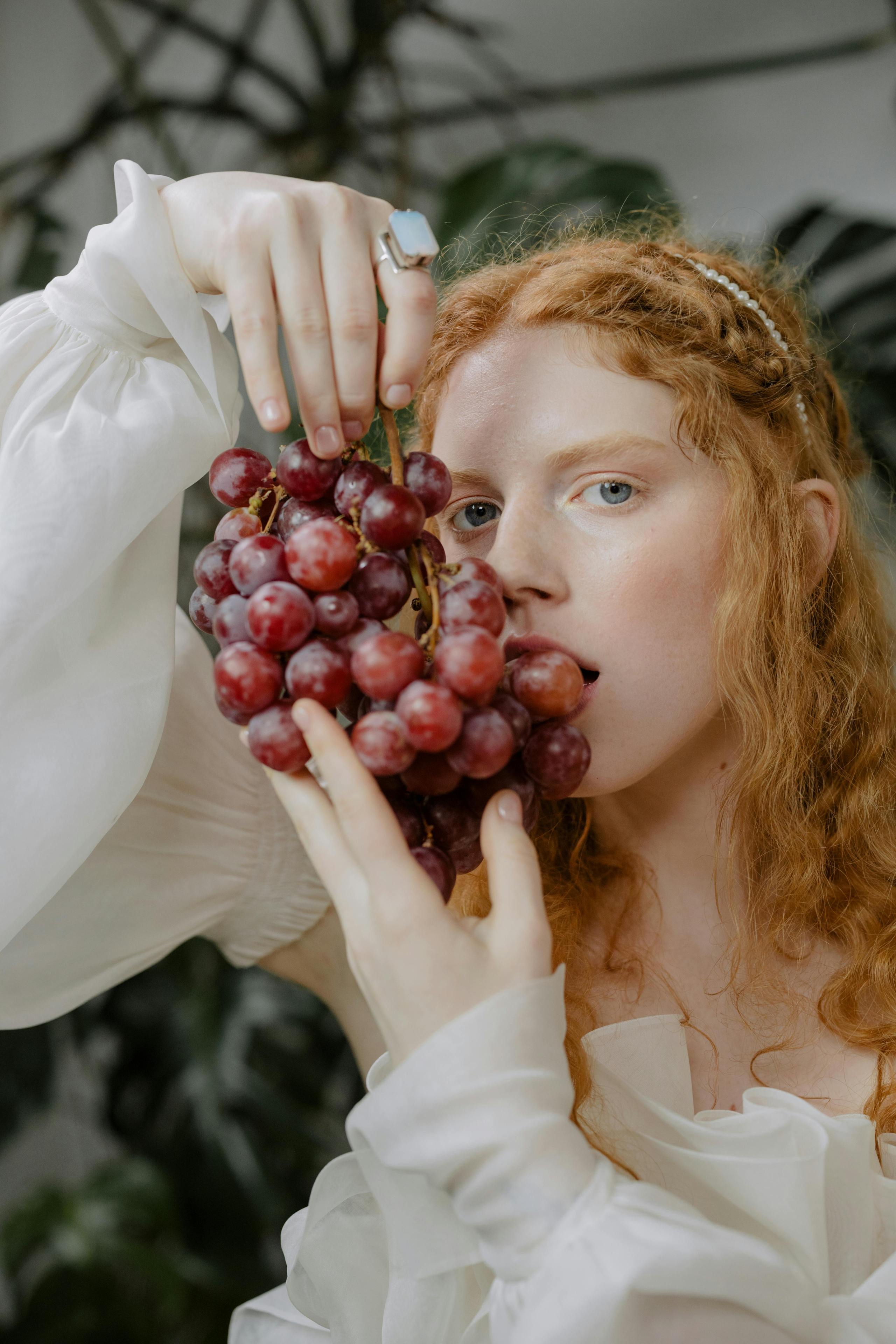 A woman holds a bunch of purple grapes to her lips, poised to eat them.
