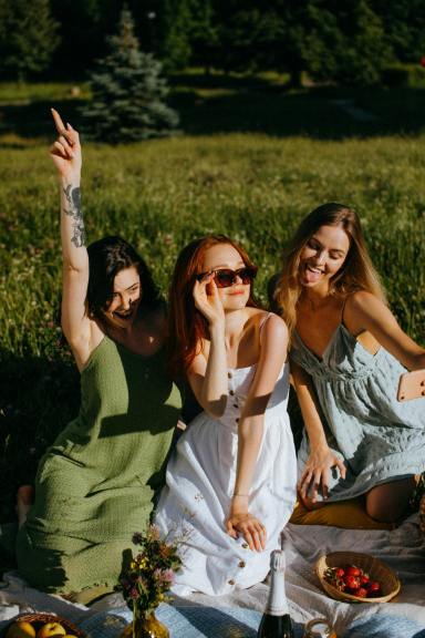 Three women sit smiling on a picnic blanket on the grass.