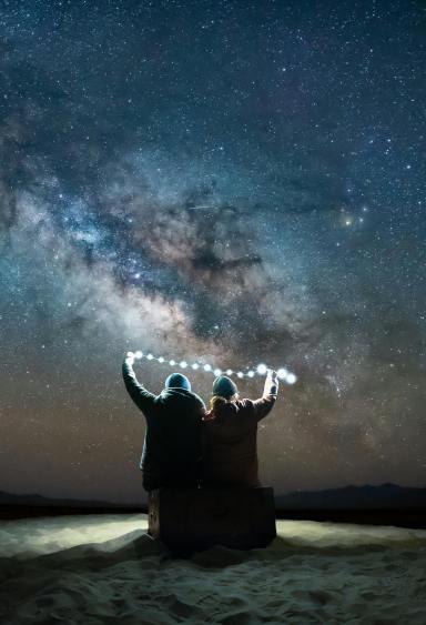 Two people watch the stars together, holding a string of lights between them.