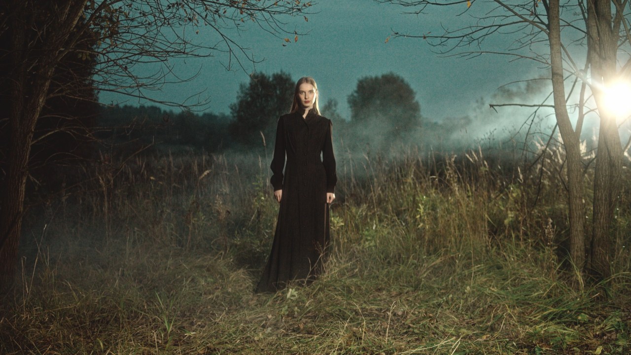 Woman in a flowing black dress standing alone in a foggy field at dusk