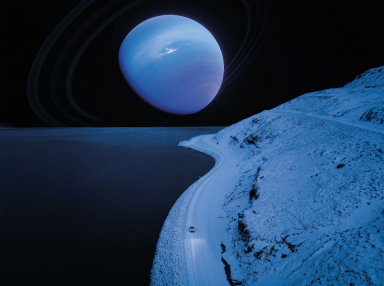 Aerial view of a lone car on a snow-covered coastal road at night with a large blue ringed planet filling the dark sky above.