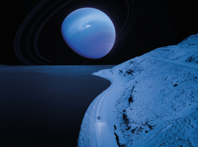 Aerial view of a lone car on a snow-covered coastal road at night with a large blue ringed planet filling the dark sky above.