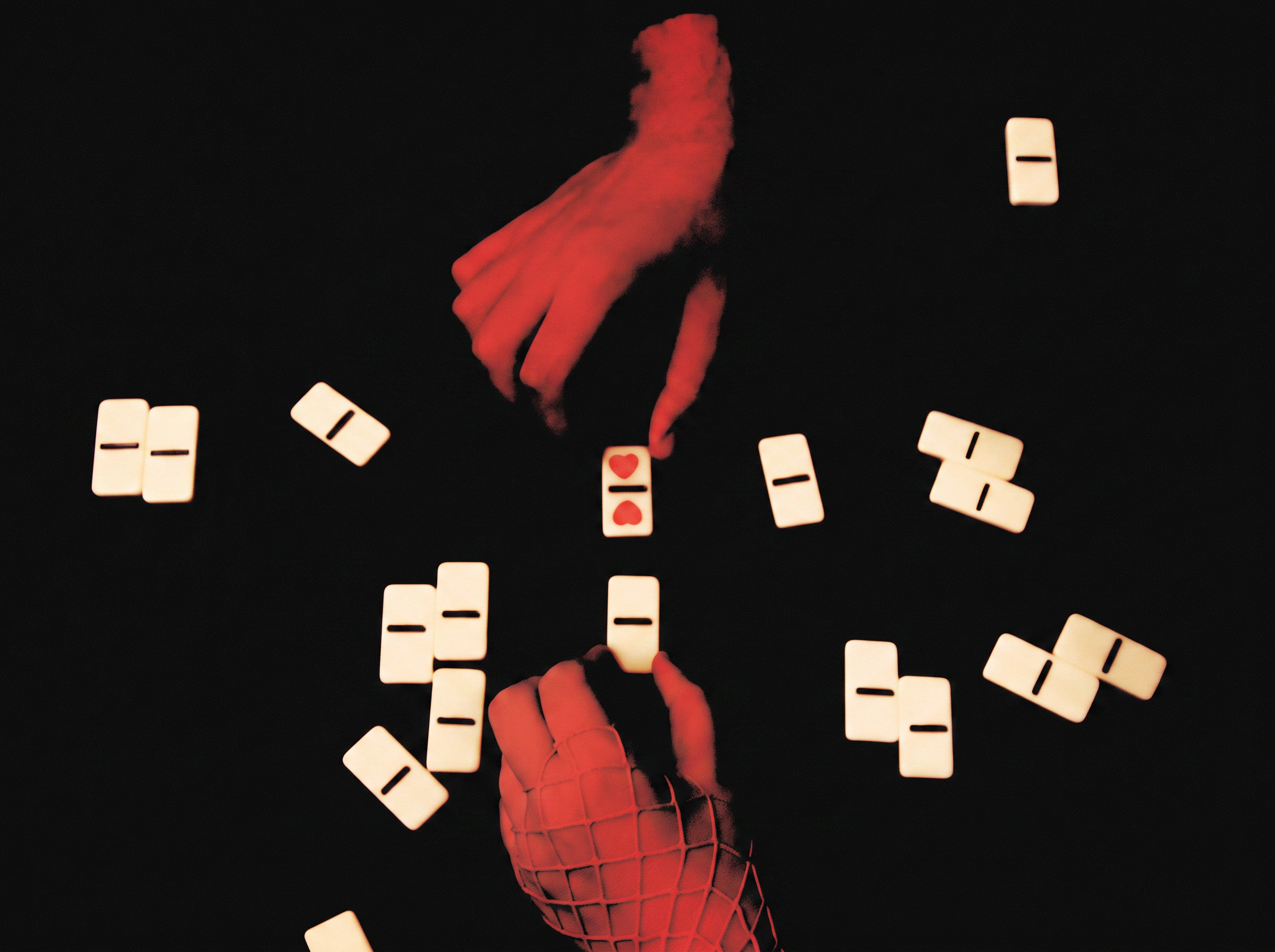 Two red-lit hands reaching toward scattered white dominoes against a black background, with one domino featuring red heart symbols.