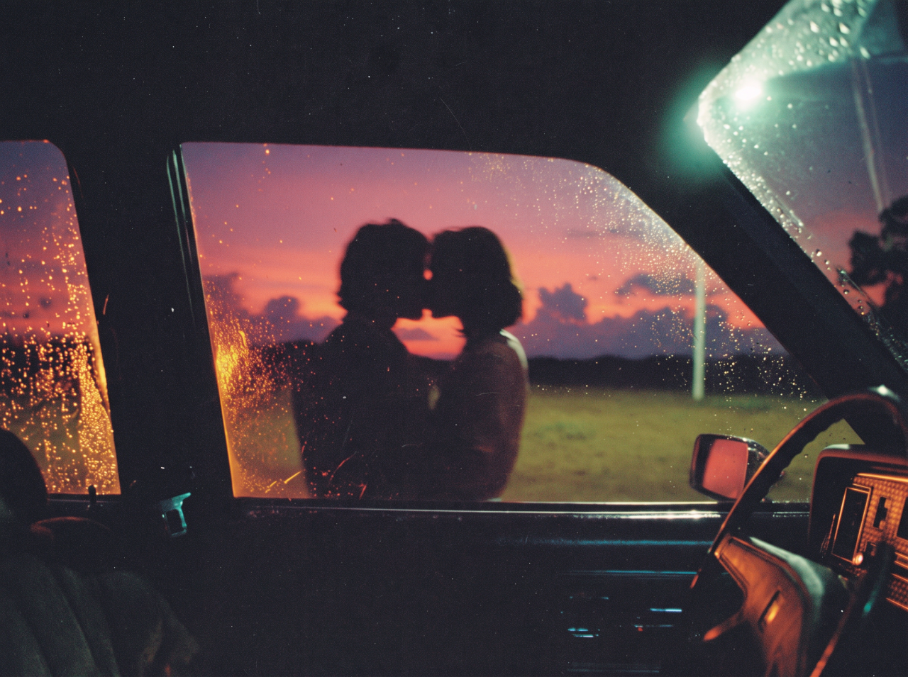Silhouettes of two people kissing outside a vintage car, framed through a rain-dotted window against a pink and orange sunset sky.