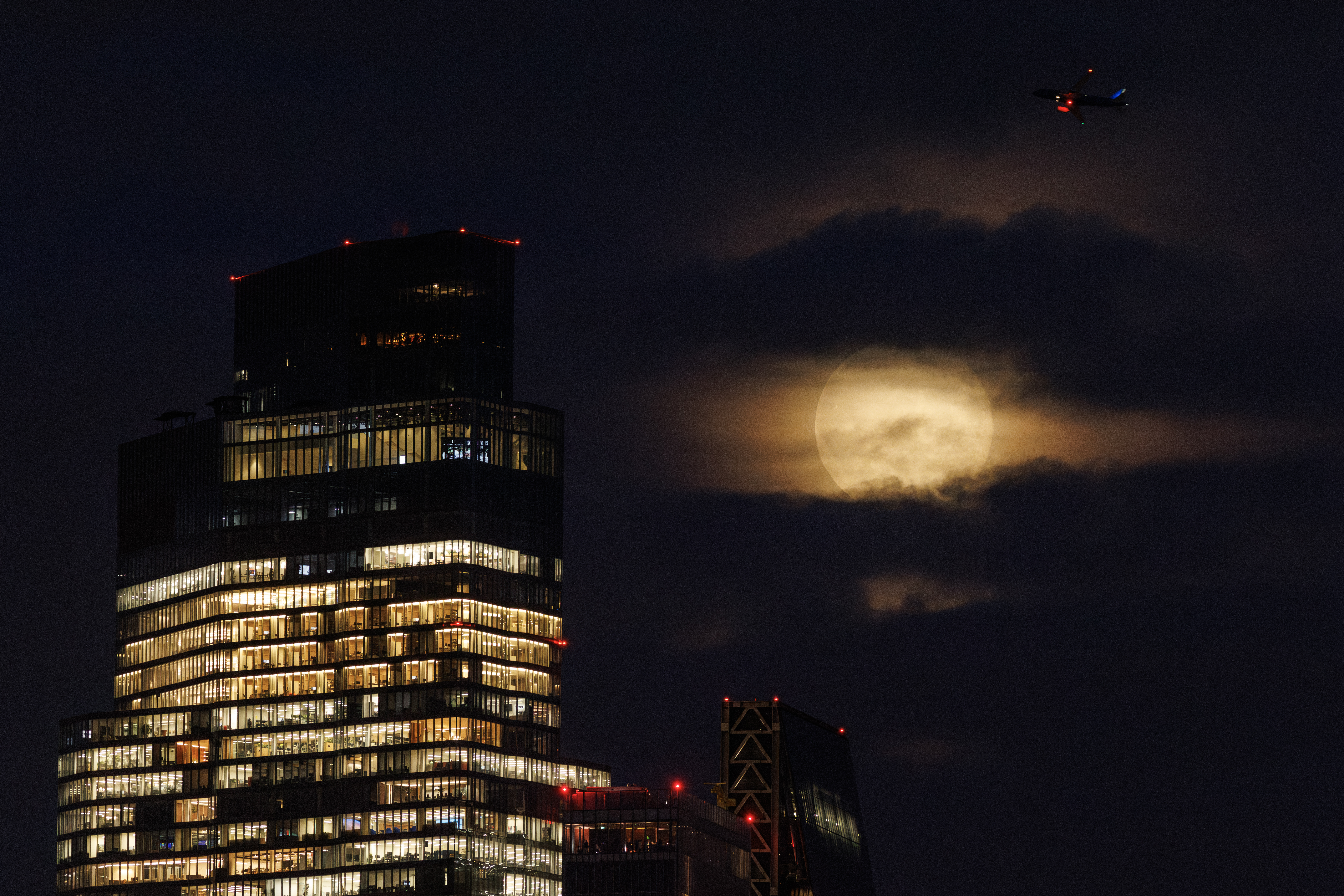 The full Harvest Moon rising above the City of London skyline at dusk