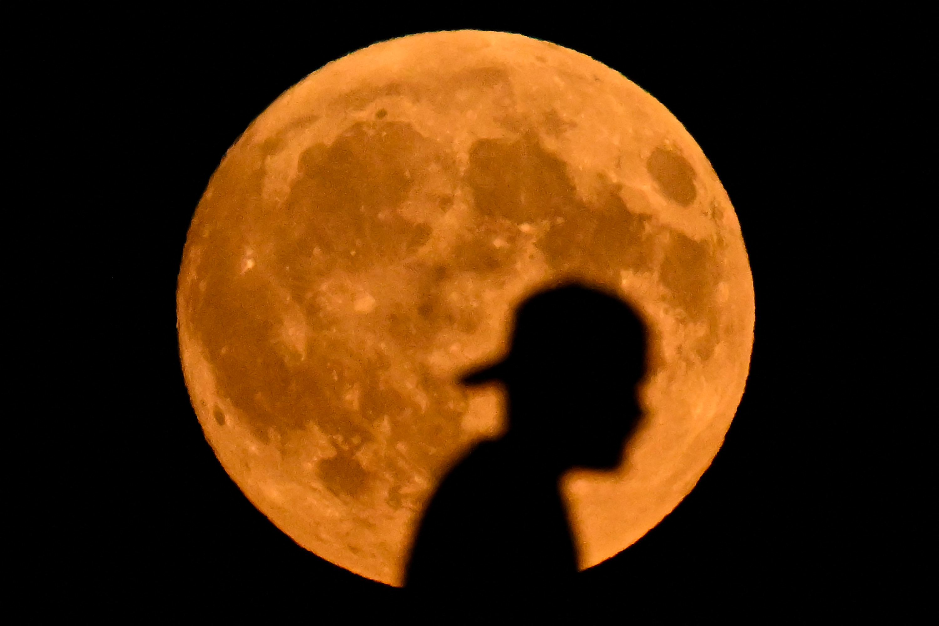 A man walks across a bridge in Frankfurt, Germany, with a large full moon looming in the background