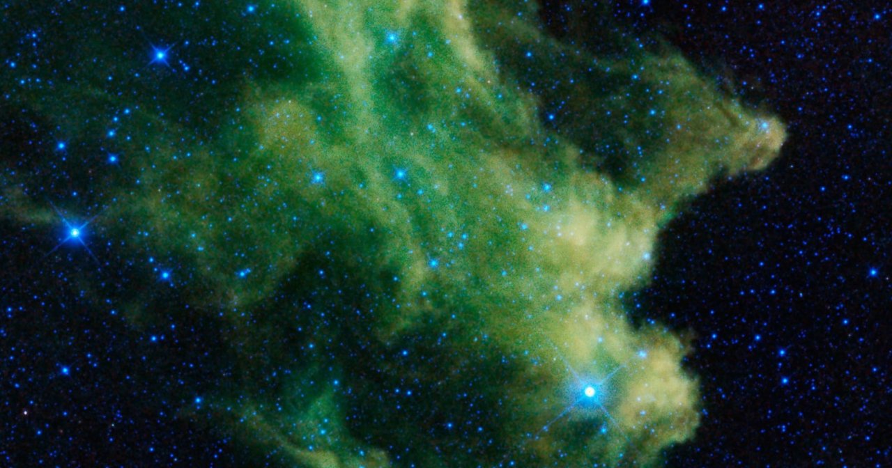 Infrared image of the Witch Head Nebula showing billowy green and yellow clouds of gas and dust amid a dark, blue-star-filled sky.
