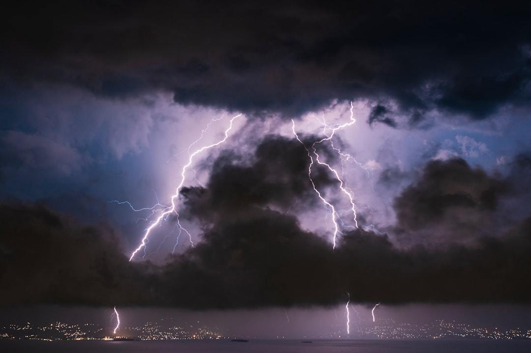 Bright lightning bolts striking behind dark storm clouds over a distant city skyline
