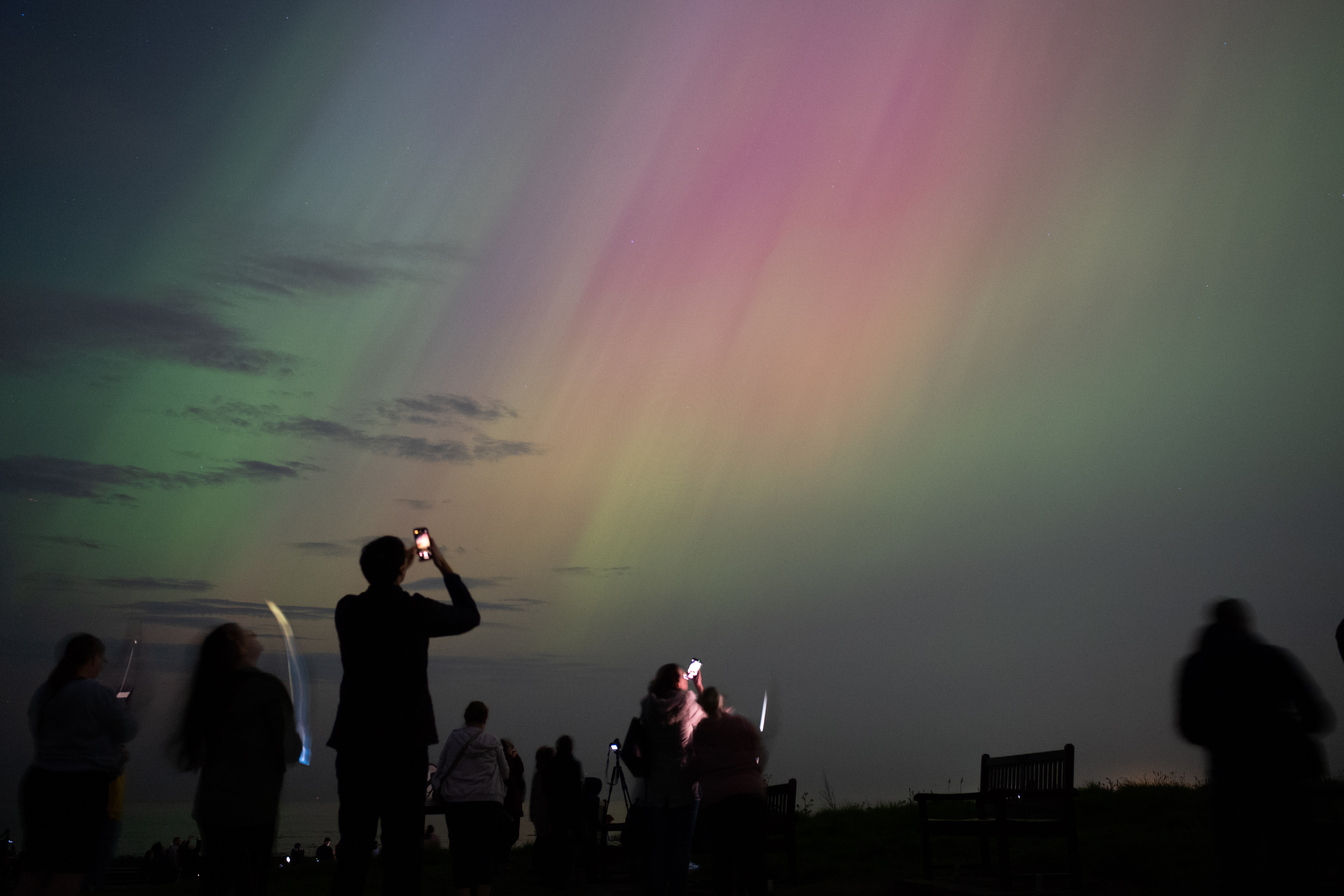 People gathered near St Mary's Lighthouse in Whitley Bay, England, watching the northern lights glow in the night sky